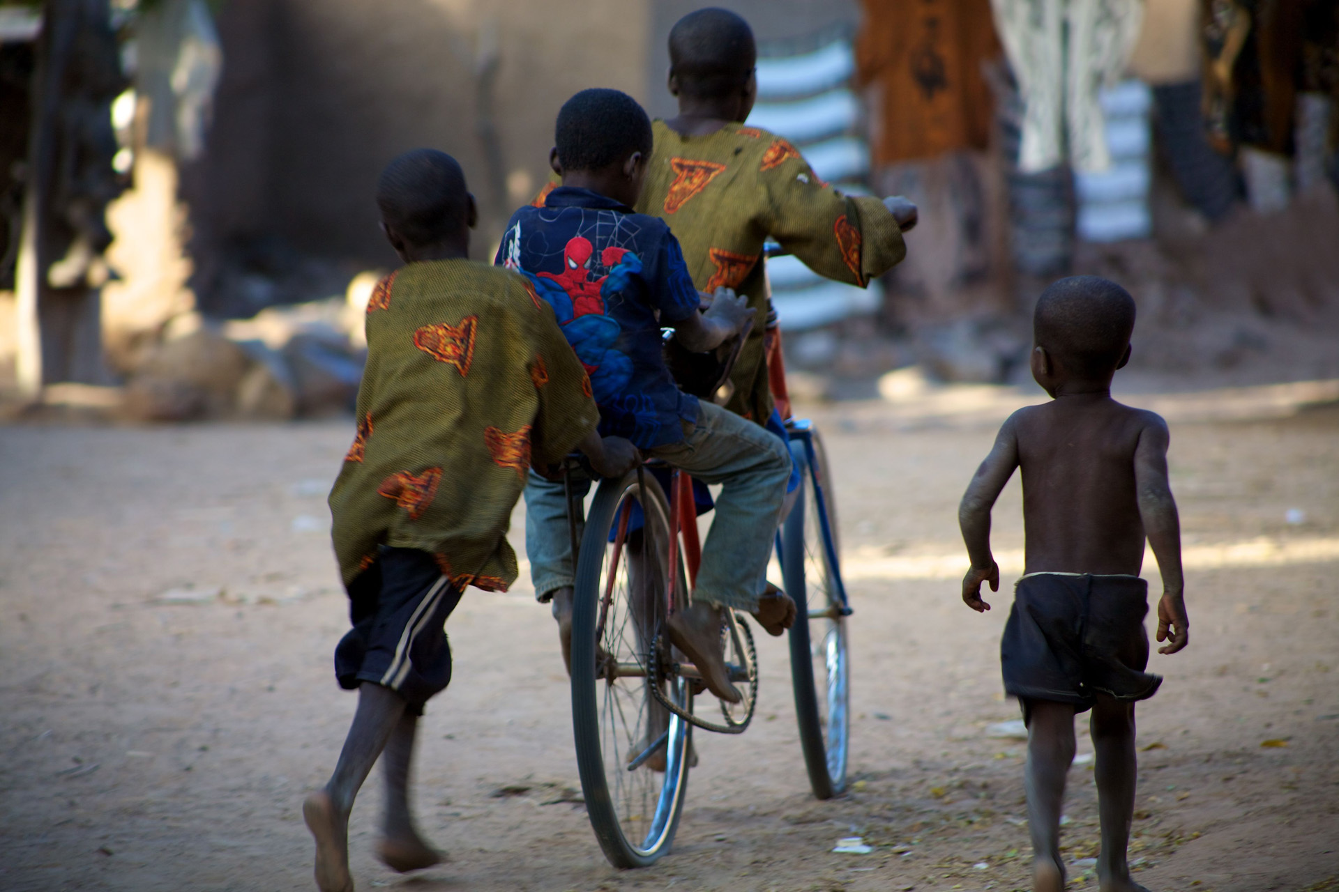 Plusieurs enfants qui jouent avec un vélo, vue de dos - Afrique